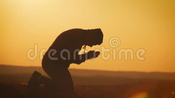 剪影的年轻人在美丽的夕阳下在外面祈祷男性寻求帮助在信仰概念宗教中找到慰藉视频的预览图