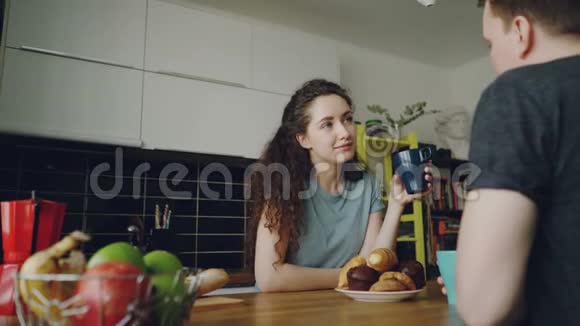 年轻的白种人夫妇坐在现代厨房的餐桌前在家里讨论一些事情卷曲的女人坐在后面视频的预览图