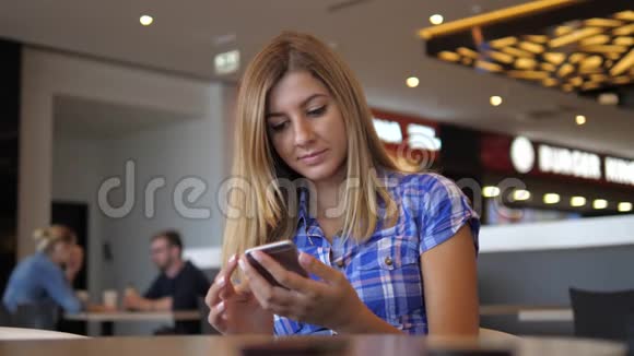 穿蓝色格子衬衫的年轻开朗的女人在咖啡厅使用智能手机视频的预览图