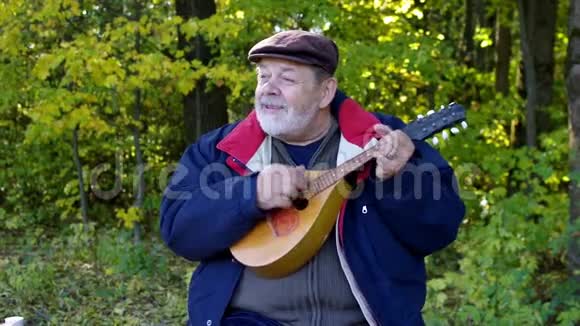 老人一边唱着曼陀林一边坐在秋林的空地上视频的预览图
