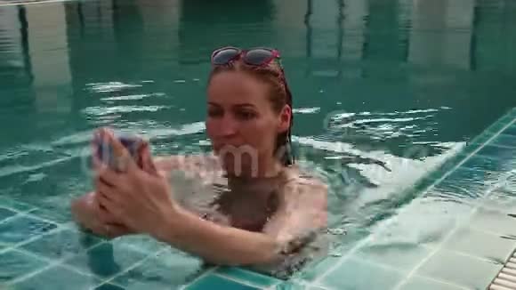 年轻女子在游泳池里放松用手机拍照视频的预览图