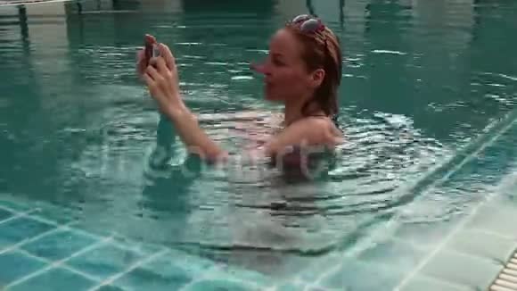 年轻女子在游泳池里放松用手机拍照视频的预览图