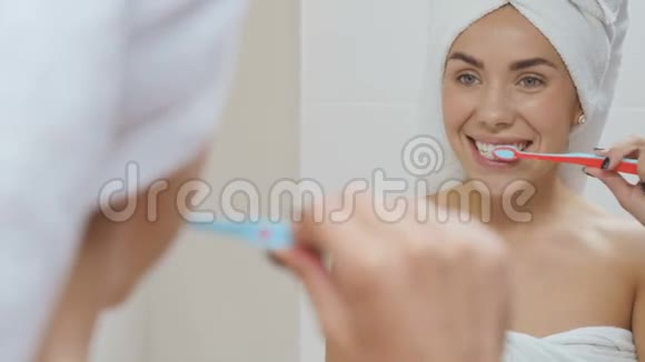 头上戴毛巾的漂亮女人在浴室镜子前刷牙视频的预览图