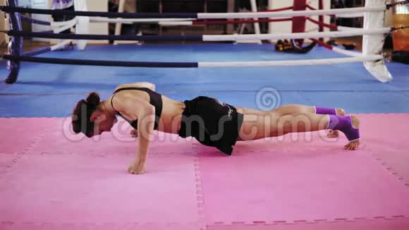 运动中的年轻女子穿着胸罩和短裤在拳击场内的运动垫上用拳头做俯卧撑视频的预览图