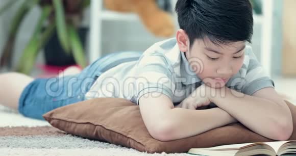 亚洲可爱的男孩在家地板上读一本书面带笑容视频的预览图