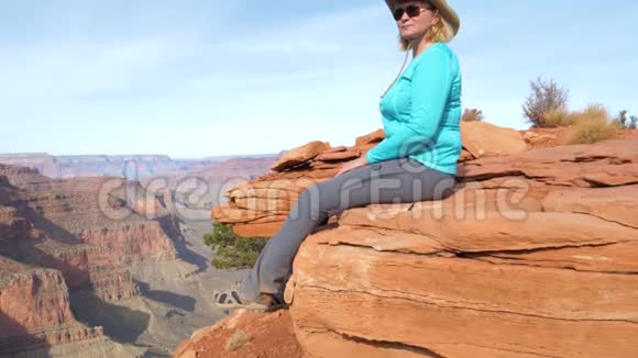 坐在岩石上晃着腿的女游客欣赏大峡谷视频的预览图
