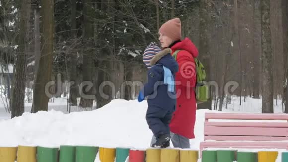 可爱的小男孩和年轻的母亲在冬天和公园里的雪玩耍蓝色的孩子夹克和红色的妈妈视频的预览图