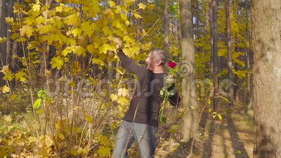 带着红玫瑰的男人在秋天的森林里等待心爱的女人的约会视频的预览图