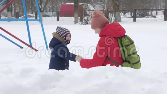 可爱的小男孩和年轻的母亲在冬天和公园里的雪玩耍蓝色的孩子夹克和红色的妈妈视频的预览图