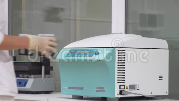 在实验室里一位身穿浴衣和手套的妇女将人体细胞样本放入离心机中的试管中视频的预览图