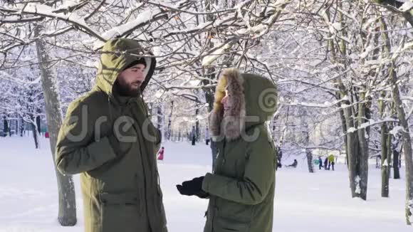 雪从树枝上落下一对夫妇用兜帽遮住他的头慢动作视频的预览图