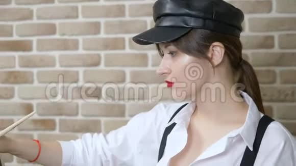 戴皮帽的女画家在画布上靠砖墙画一幅画视频的预览图