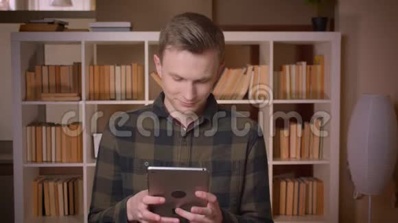 在大学图书馆里用平板电脑拍摄年轻有魅力的高加索男学生的特写镜头视频的预览图