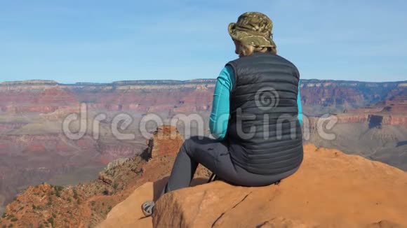 坐在岩石上晃着腿的女游客欣赏大峡谷视频的预览图