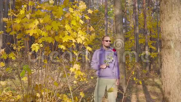 带着红玫瑰的男人在秋天的森林里等待心爱的女人的约会视频的预览图