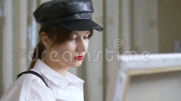 戴皮帽的女画家在画布上靠砖墙画一幅画视频的预览图