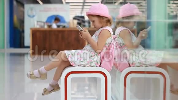 在机场候机楼里坐在等候室里的儿童游客在等待他们的时候玩手机视频的预览图