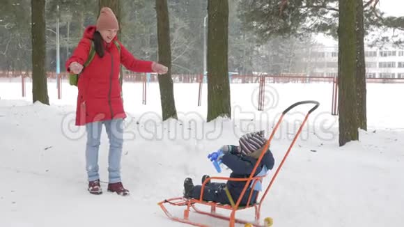 可爱的小男孩和年轻的母亲在冬天和公园里的雪玩耍蓝色的孩子夹克和红色的妈妈视频的预览图