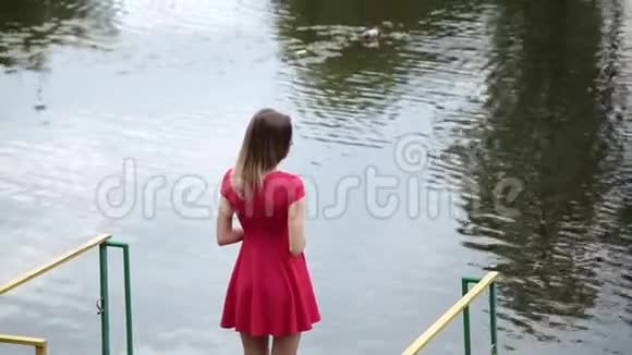 一个穿红色衣服的非常漂亮的女孩站在一个小湖附近的码头上视频的预览图