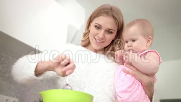 年轻的妈妈手里拿着婴儿做饭婴儿营养烹饪视频的预览图