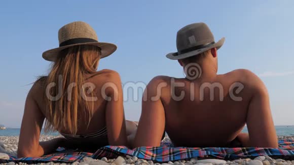 幸福的年轻夫妇在海边的海滩上晒日光浴躺在后面视频的预览图