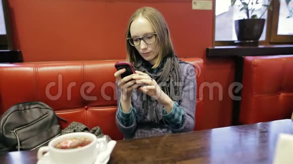 漂亮的女人戴着眼镜在智能手机上使用应用程序在咖啡馆里微笑在手机上发短信漂亮的年轻休闲装视频的预览图