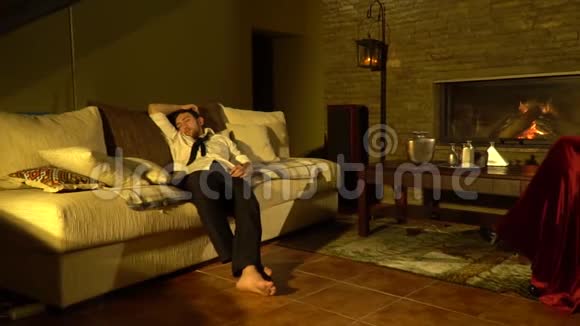 一个穿着西装的疲惫的男人睡在沙发上一个穿着红色连衣裙的女人坐在壁炉旁的椅子上视频的预览图