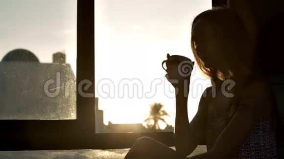 女孩剪影在明亮的窗户边喝咖啡视频的预览图