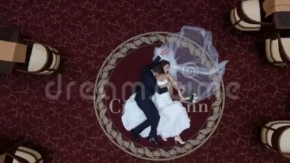 躺在豪华酒店的红地毯上拥抱新婚夫妇新郎温柔地亲吻新娘移动摄像机视频的预览图