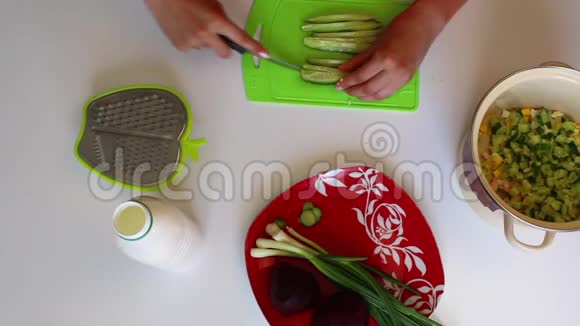 一个女人正在切切割板上的黄瓜盘子旁边是蔬菜汤煮甜菜和洋葱的其他原料视频的预览图