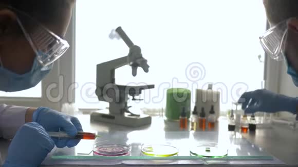 现代医学女性带男性进入护目镜和橡胶手套在培养皿中进行化学实验视频的预览图