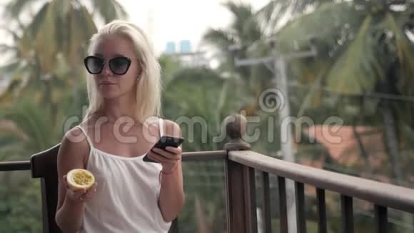 女孩在度假时在酒店咖啡厅喝果汁检查手机以看到大海和海滩的激情视频的预览图