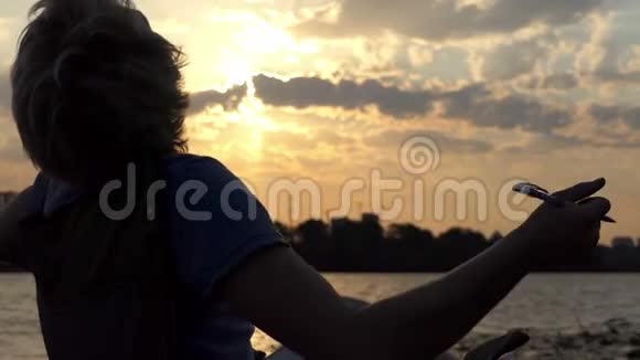 年轻男子在河岸上伸展自己的折叠椅在日落时写作视频的预览图