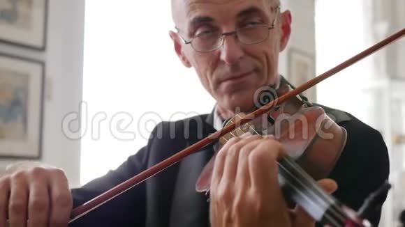 小提琴家的肖像戴眼镜的老人在木制小提琴上演奏视频的预览图
