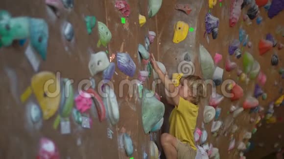 一个小男孩在一个巨石攀爬体育馆里爬墙时慢镜头视频的预览图