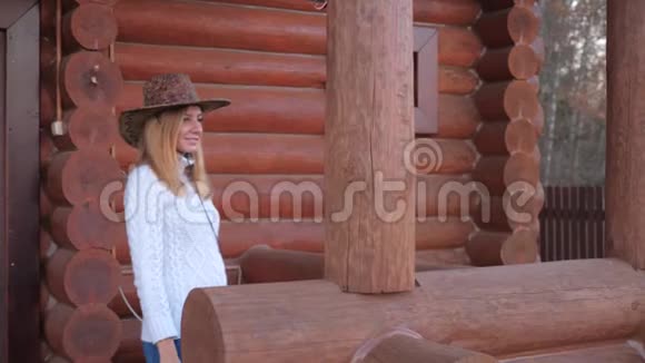 穿着白色毛衣戴着牛仔帽的漂亮女人在木屋的阳台上视频的预览图
