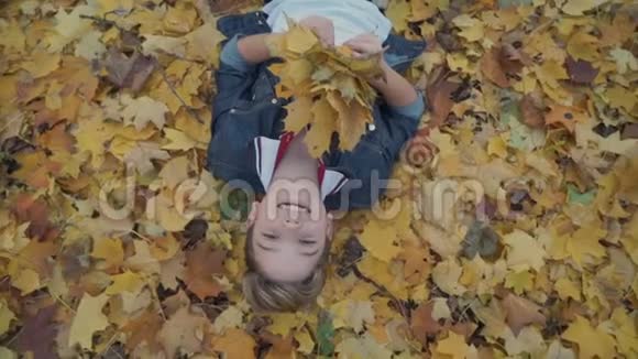 带着一束叶子的快乐男孩躺在黄色的叶子上视频的预览图