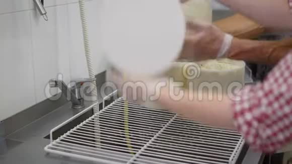 两个奶酪制造商在工厂的房间里成型的过程中把奶酪头放在碗里戴着防护用品视频的预览图