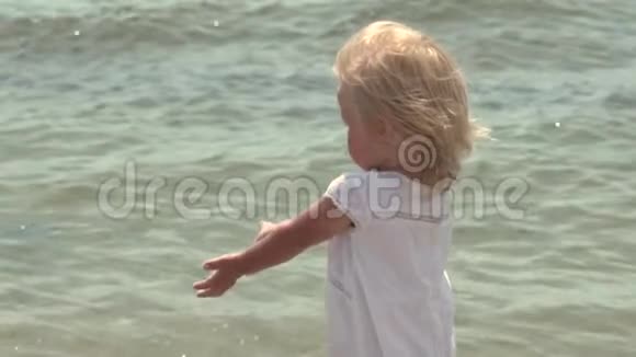 美丽的小女孩沿着海滨散步在海岸穿白色裙子的小女孩慢动作视频的预览图