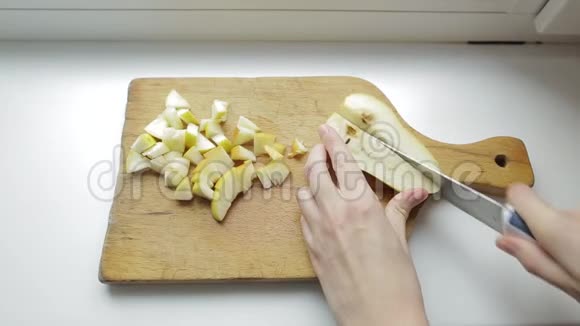 年轻女孩雕刻着一个新鲜有机梨的核心女人在白色背景的木制厨房板上切梨视频的预览图
