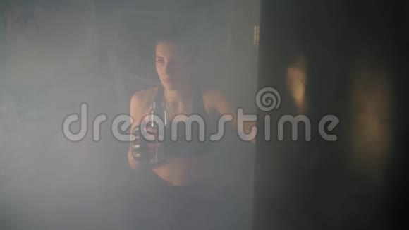 口渴的女拳击手在黑暗的健身房里抽烟训练后从水瓶里休息喝酒美丽美丽视频的预览图