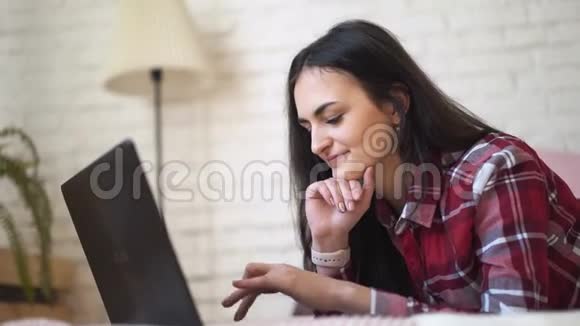 年轻女子在家工作手提电脑穿着格子衬衫靠着砖墙背景视频的预览图