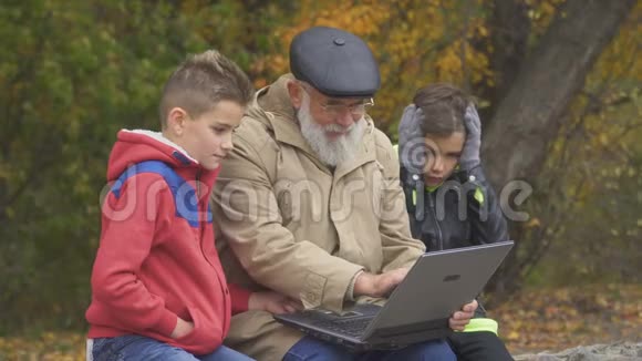 祖父的孙子们在秋天公园用笔记本电脑视频的预览图