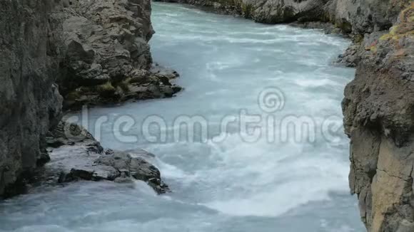 冰岛的山脉河流流经两块黑色岩石蓝色冰川水视频的预览图