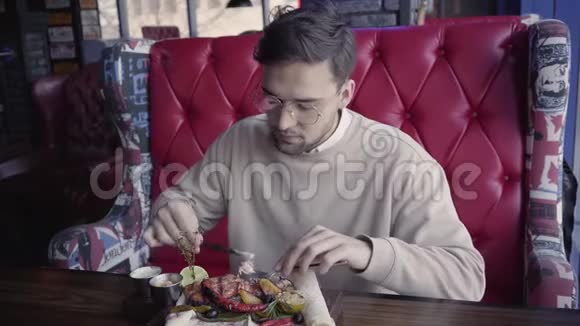 帅哥坐在豪华餐厅里吃着美味可口的菜肴和烤肉和蔬菜视频的预览图