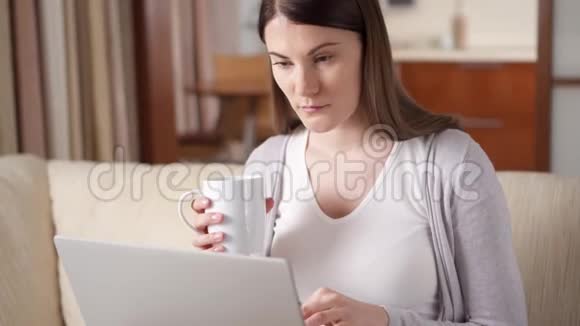昏昏欲睡的打哈欠的职业妇女在家里用笔记本电脑喝咖啡家庭办公概念视频的预览图