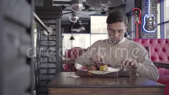 帅哥坐在豪华餐厅里吃着美味可口的菜肴和烤肉和蔬菜视频的预览图