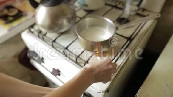 一个年轻的女人在厨房里用火柴点燃一个煤气灶女孩在平底锅里加热牛奶做燕麦烹饪视频的预览图