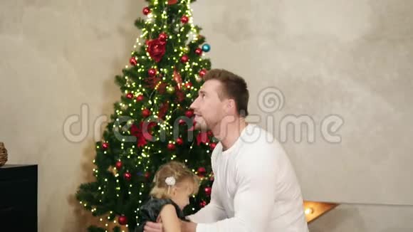 年轻的父亲用装饰好的圣诞树把他可爱的女儿扔在家中的慢镜头视频的预览图