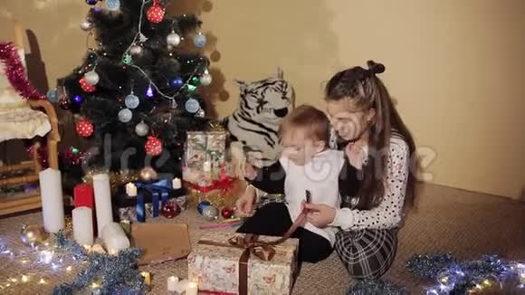 小男孩带着妹妹在一棵装饰精美的圣诞树旁打开新年礼盒视频的预览图